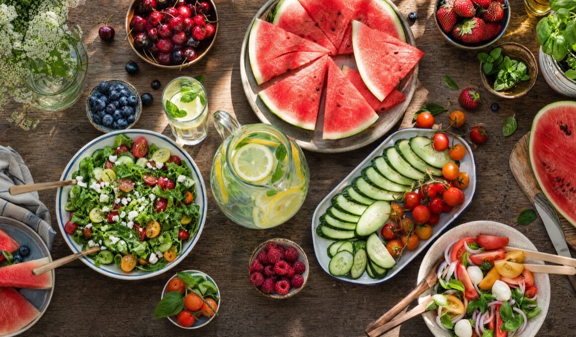 Tisch voller kuehlender Sommer-Lebensmittel wie Wassermelone Gurke und Salat