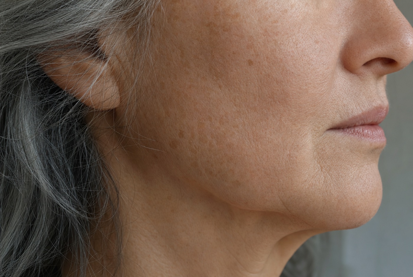 Close-up of the cheek and jawline of a woman in her early sixties in soft daylight showing natural skin texture